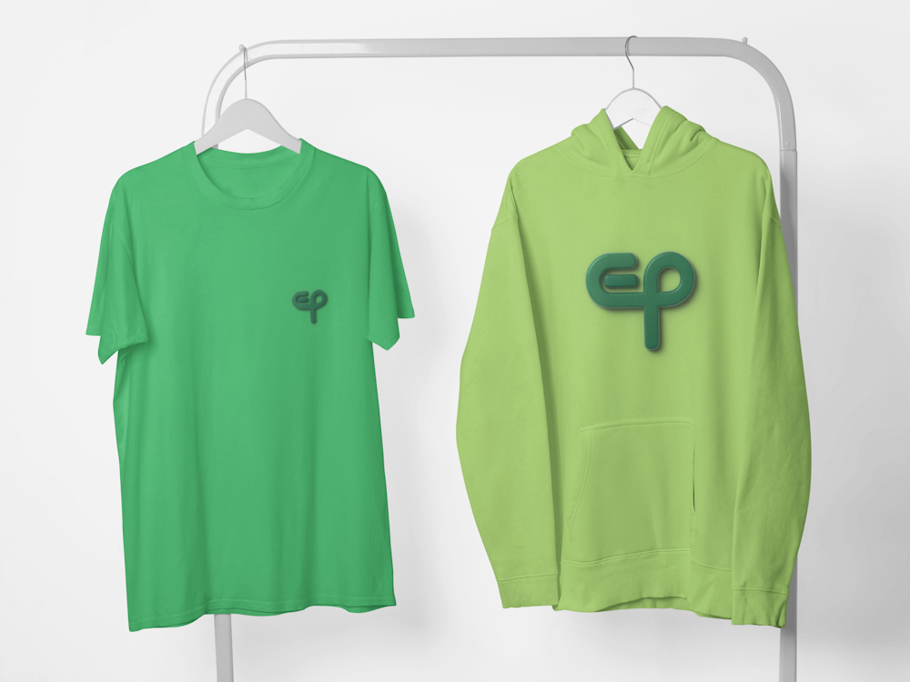 Zelena pamučna majica okruglog izreza oko vrata s logom i majica sportska s kapuljačom i logom vise na vješalici na svijetloj pozadini